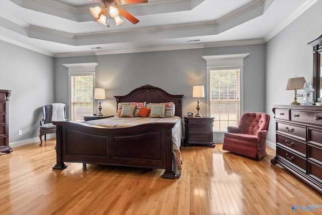 bedroom with a raised ceiling, multiple windows, and light wood-type flooring