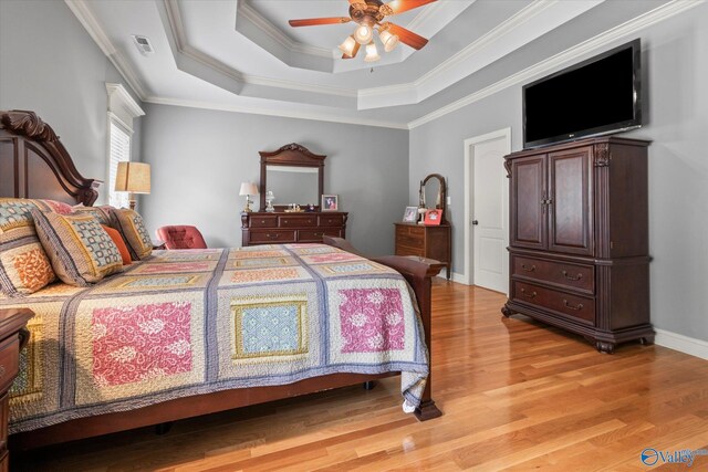 bedroom featuring ceiling fan, crown molding, light wood-type flooring, and a tray ceiling