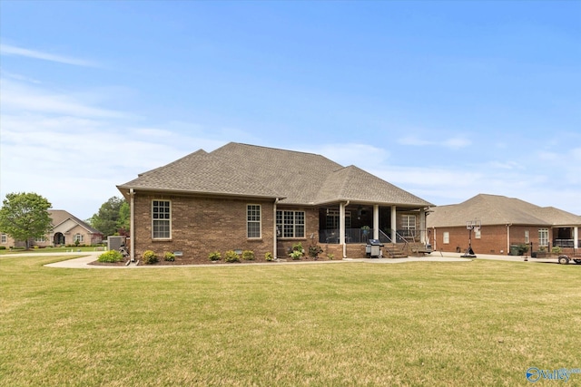 back of house with a shingled roof, a porch, brick siding, and a yard