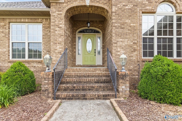 entrance to property featuring brick siding and a shingled roof
