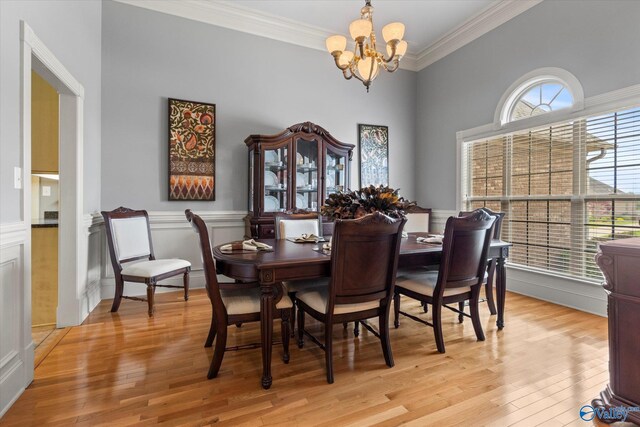 dining room with a wainscoted wall, a notable chandelier, light wood-style floors, and ornamental molding