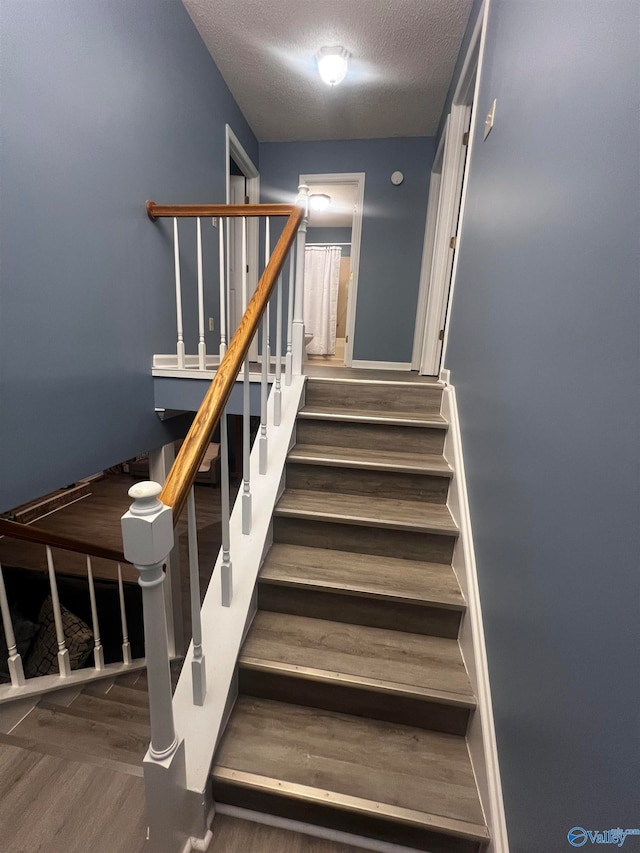 staircase with a textured ceiling and wood finished floors