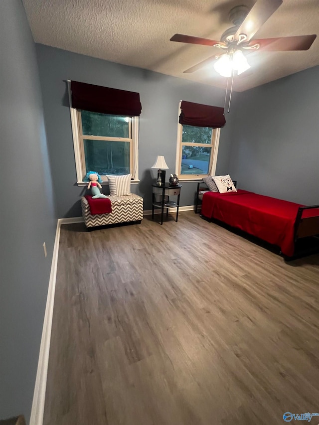 bedroom with a ceiling fan, a textured ceiling, baseboards, and wood finished floors