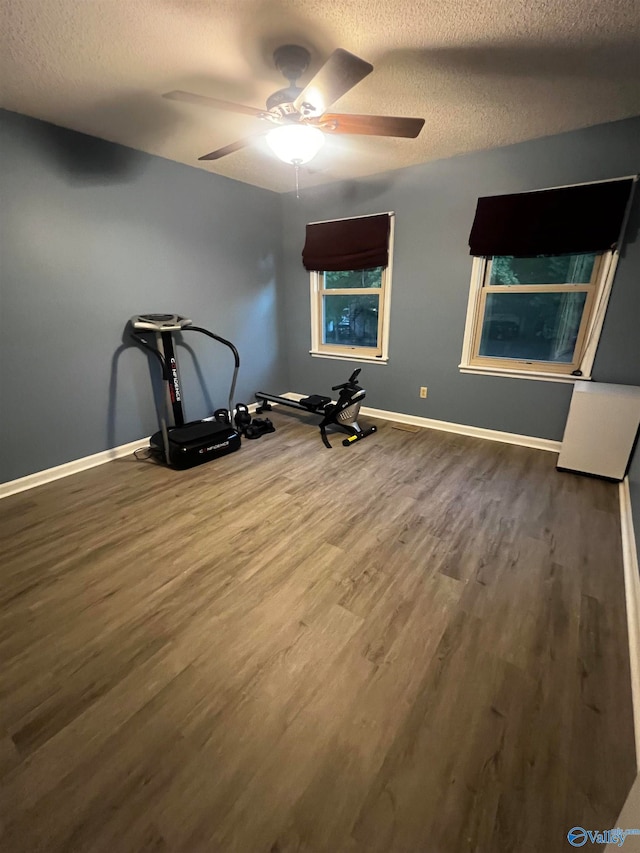 exercise room with ceiling fan, a textured ceiling, baseboards, and wood finished floors