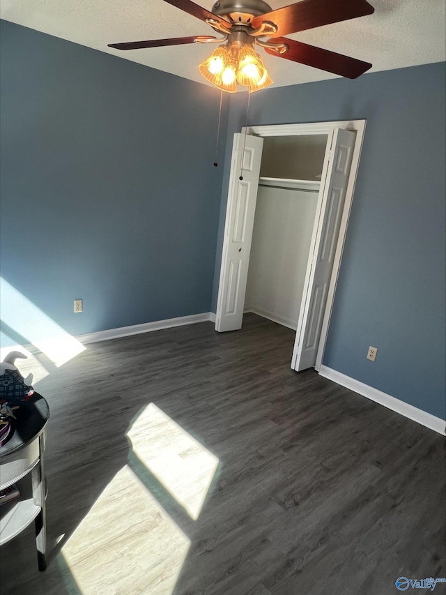 unfurnished bedroom with ceiling fan, a textured ceiling, baseboards, a closet, and dark wood finished floors