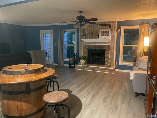 living area featuring a brick fireplace, baseboards, ornamental molding, and wood finished floors