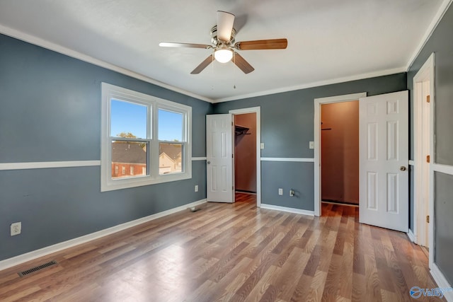 unfurnished bedroom featuring crown molding, ceiling fan, a walk in closet, wood-type flooring, and a closet