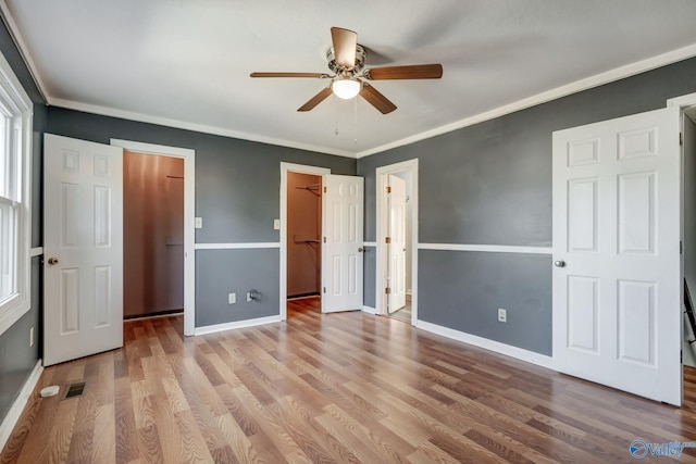 unfurnished bedroom with crown molding, a walk in closet, light wood-type flooring, and ceiling fan