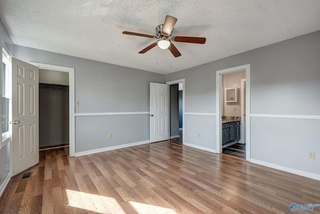 unfurnished bedroom with wood-type flooring, ceiling fan, connected bathroom, and a closet