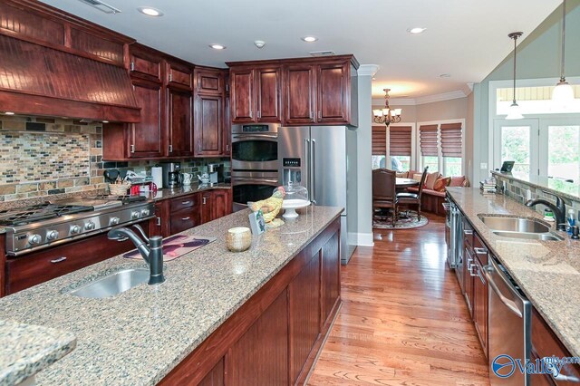 kitchen with light wood-type flooring, light stone counters, appliances with stainless steel finishes, sink, and ornamental molding