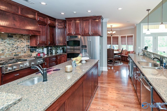 kitchen featuring sink, premium range hood, hanging light fixtures, stainless steel appliances, and light stone counters