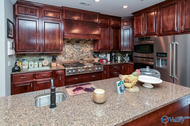 kitchen featuring decorative backsplash, light stone countertops, stainless steel appliances, and custom range hood