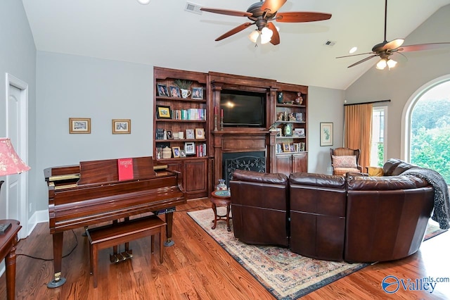 living room with lofted ceiling, light hardwood / wood-style floors, built in shelves, and ceiling fan