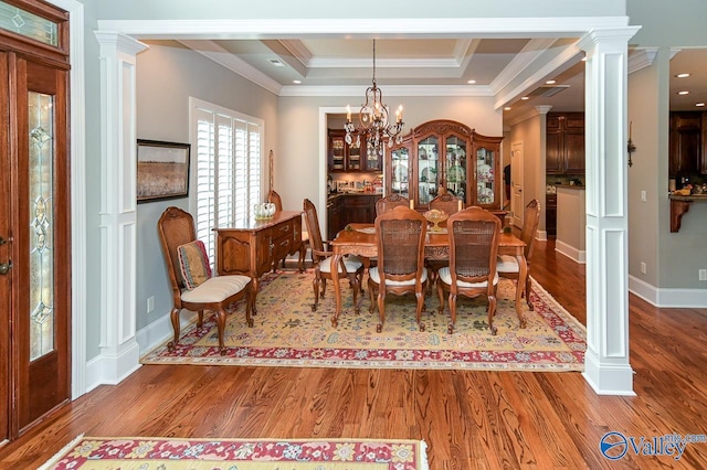 dining space with wood-type flooring, a tray ceiling, decorative columns, and a notable chandelier