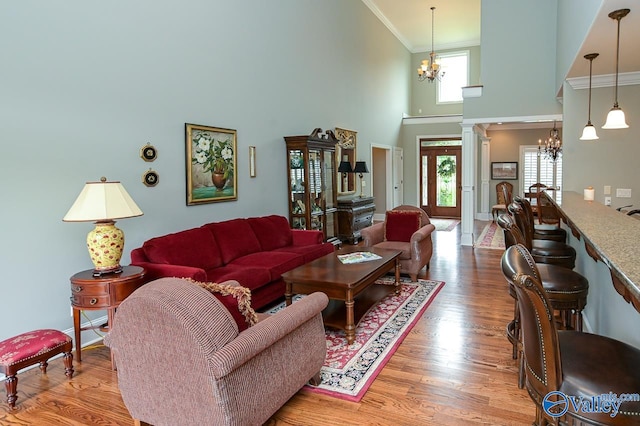 living room featuring a chandelier, crown molding, high vaulted ceiling, decorative columns, and light hardwood / wood-style floors