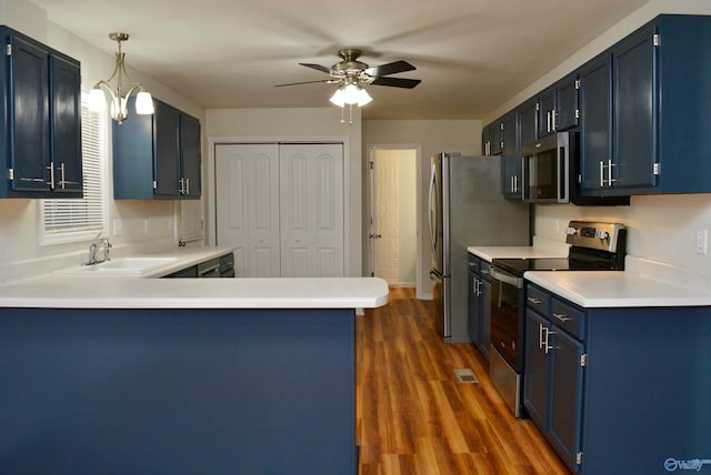 kitchen featuring dark wood-type flooring, kitchen peninsula, sink, blue cabinetry, and appliances with stainless steel finishes