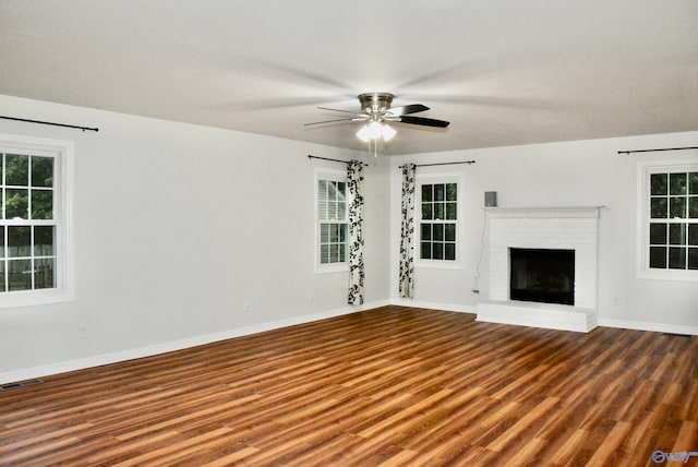 unfurnished living room featuring ceiling fan, wood-type flooring, a brick fireplace, and plenty of natural light