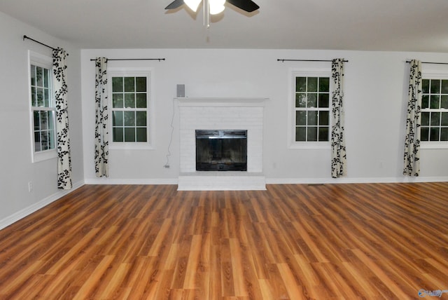 unfurnished living room with ceiling fan, a healthy amount of sunlight, a brick fireplace, and hardwood / wood-style floors