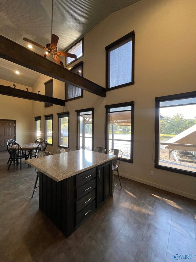 kitchen with ceiling fan, vaulted ceiling with beams, a kitchen breakfast bar, and a center island