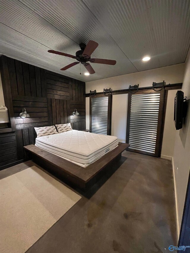 unfurnished bedroom featuring ceiling fan, wooden walls, a barn door, and carpet