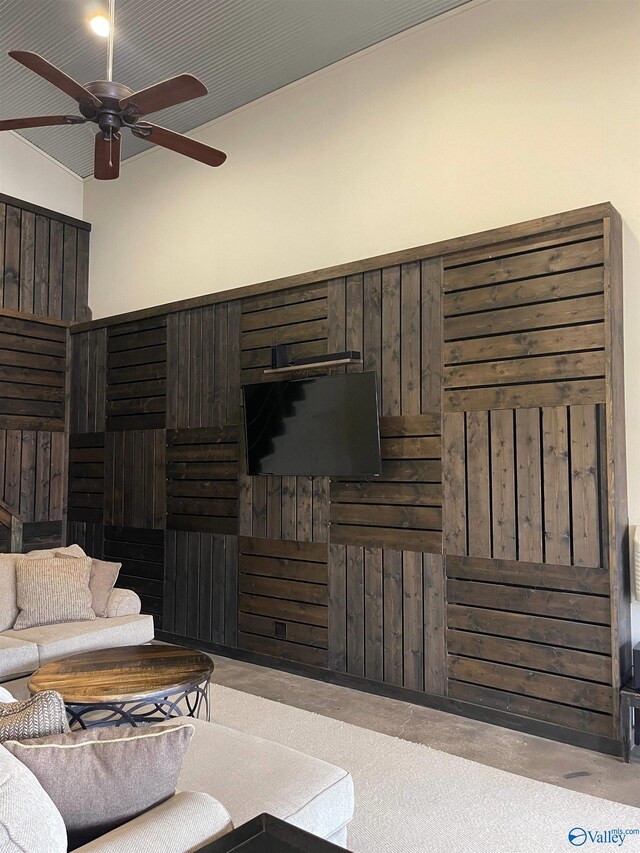 living room featuring wooden walls, ceiling fan, and a high ceiling