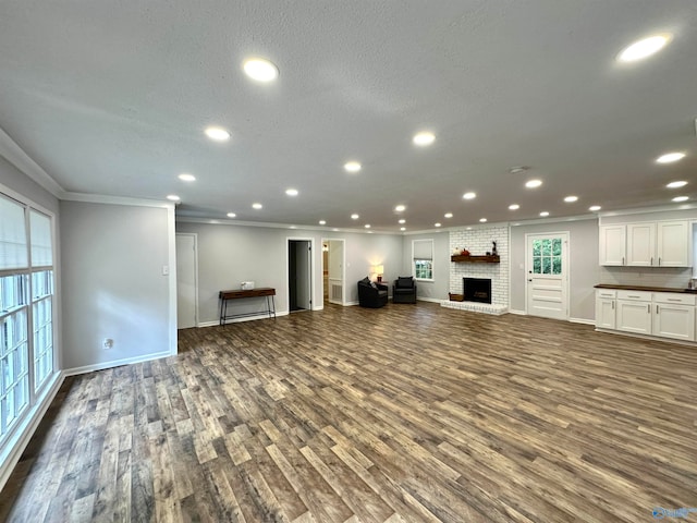 unfurnished living room with a brick fireplace, a textured ceiling, dark hardwood / wood-style floors, and crown molding