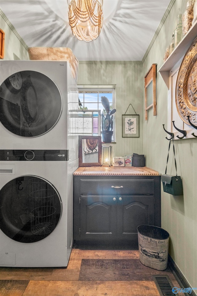 laundry area featuring stacked washer and clothes dryer, ornamental molding, hardwood / wood-style floors, and cabinets