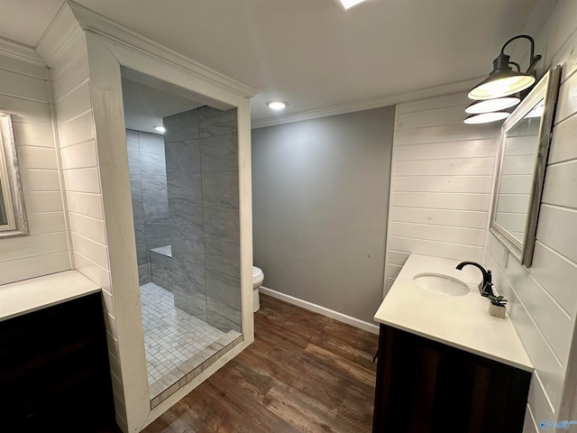 bathroom featuring hardwood / wood-style flooring, toilet, tiled shower, vanity, and crown molding