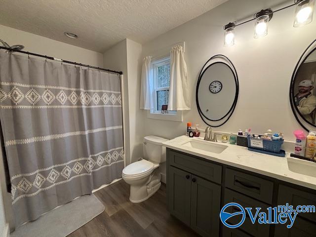 bathroom with toilet, a textured ceiling, vanity, wood finished floors, and a shower with curtain