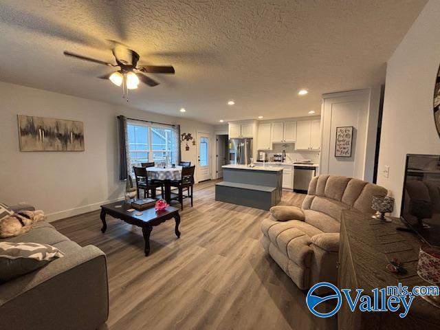 living room featuring recessed lighting, light wood-style floors, a ceiling fan, a textured ceiling, and baseboards