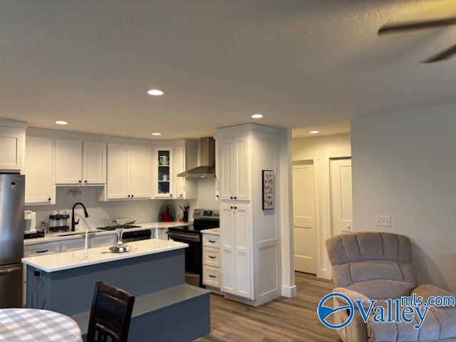 kitchen featuring stainless steel appliances, a sink, light countertops, wall chimney exhaust hood, and glass insert cabinets