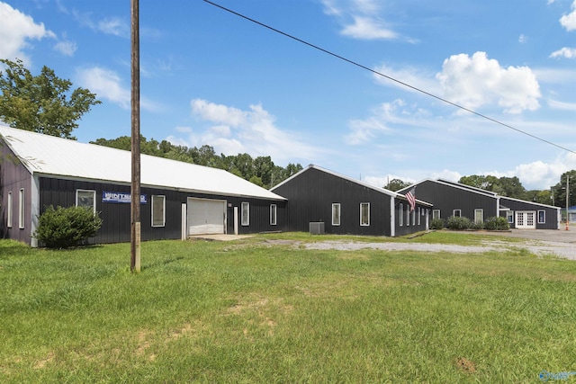 view of front of house with a pole building, a front yard, central AC unit, a garage, and an outdoor structure