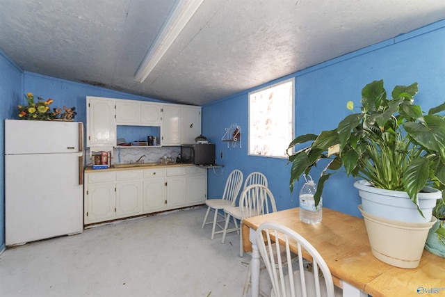 kitchen with white cabinetry, lofted ceiling, concrete floors, and freestanding refrigerator