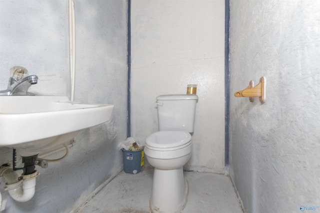 half bathroom featuring a sink, toilet, and concrete flooring