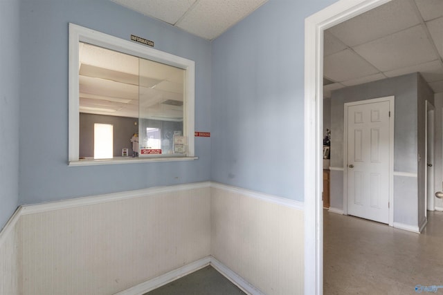 corridor featuring a paneled ceiling and a wainscoted wall