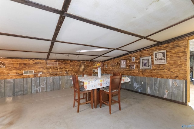 dining space with visible vents, wood walls, concrete flooring, and vaulted ceiling