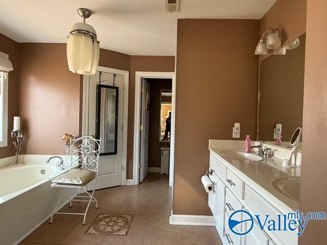 bathroom featuring baseboards, double vanity, a sink, tile patterned flooring, and a garden tub