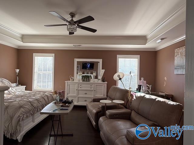 bedroom with visible vents, a raised ceiling, wood finished floors, and ornamental molding