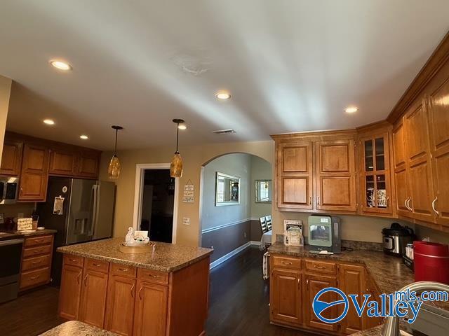 kitchen with dark wood-style flooring, arched walkways, appliances with stainless steel finishes, and brown cabinets