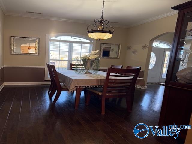 dining area featuring dark wood-style floors, visible vents, baseboards, arched walkways, and ornamental molding