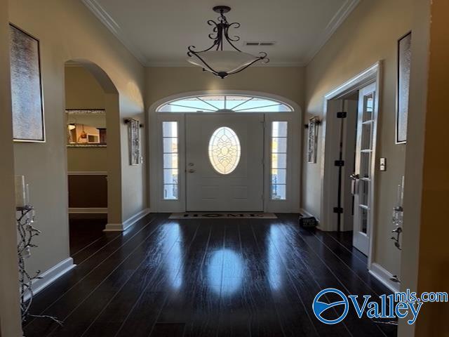 foyer with wood finished floors, visible vents, baseboards, arched walkways, and ornamental molding