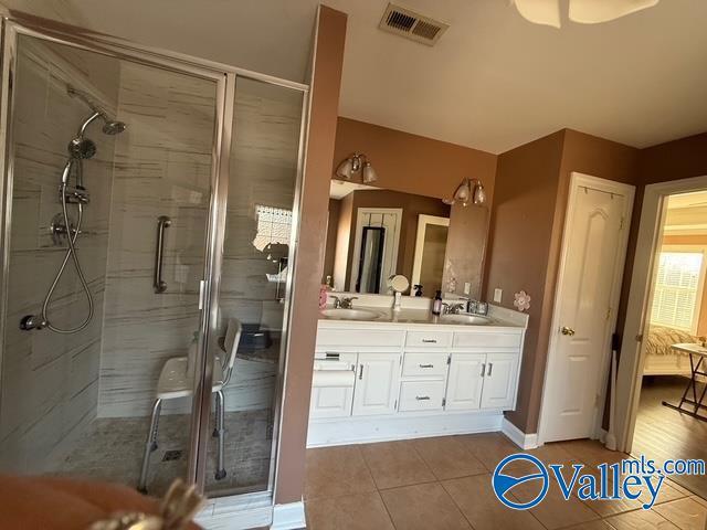 full bath with visible vents, a shower stall, double vanity, tile patterned floors, and a sink