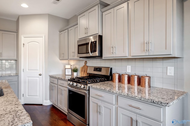 kitchen featuring tasteful backsplash, light stone counters, dark hardwood / wood-style floors, and appliances with stainless steel finishes