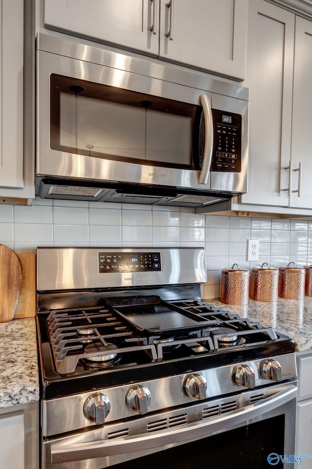 kitchen featuring decorative backsplash, light stone counters, gray cabinets, and stainless steel appliances