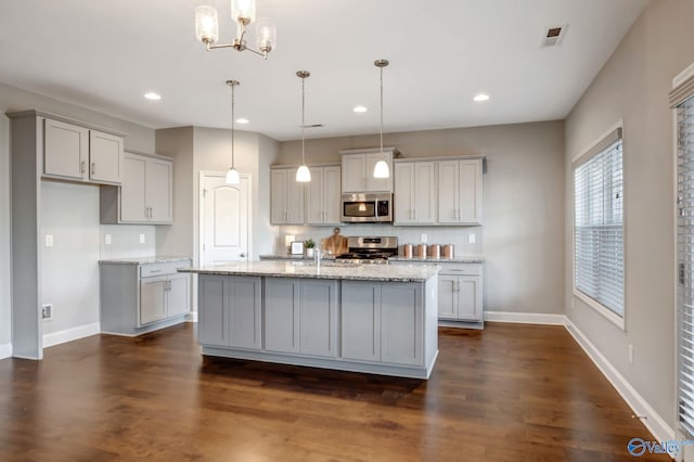 kitchen with decorative backsplash, decorative light fixtures, and a kitchen island with sink