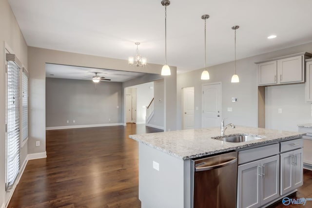 kitchen featuring light stone counters, stainless steel dishwasher, an island with sink, pendant lighting, and ceiling fan with notable chandelier