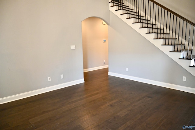 unfurnished room with arched walkways, stairway, wood finished floors, and baseboards