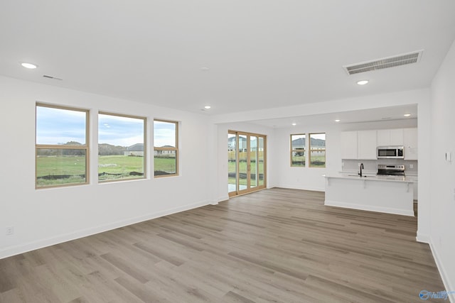 unfurnished living room featuring plenty of natural light, sink, and light hardwood / wood-style flooring