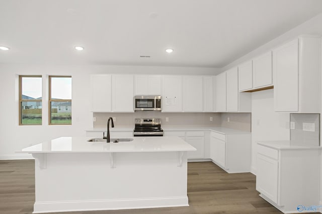 kitchen with stainless steel appliances, an island with sink, sink, and white cabinets