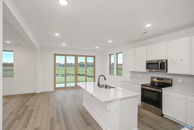 kitchen with an island with sink, white cabinetry, sink, stainless steel appliances, and french doors